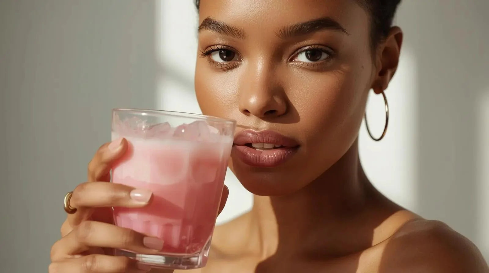Femme avec peau lumineuse tenant un verre de boisson rose glacée, soins peau ADISAEL