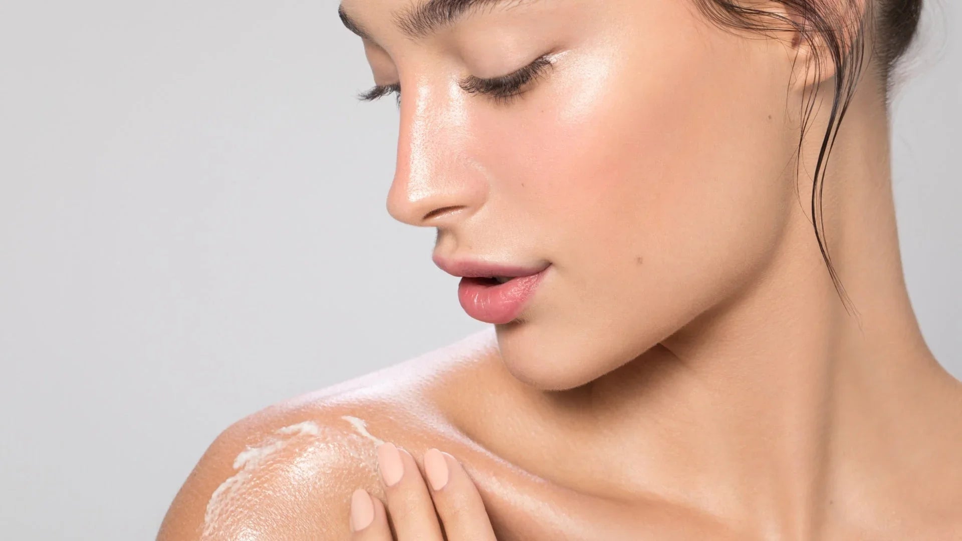 Femme appliquant une crème hydratante sur l'épaule, peau lumineuse et éclatante